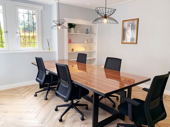 Een vergaderruimte met een glanzende houten tafel, zwarte bureaustoelen en design lampen.