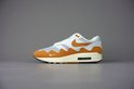 Rechter Nike Air Max 1 Patta sneaker in wit, oranje, beige en bruin, op een grijze achtergrond.