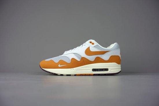 Rechter Nike Air Max 1 Patta sneaker in wit, oranje, beige en bruin, op een grijze achtergrond.
