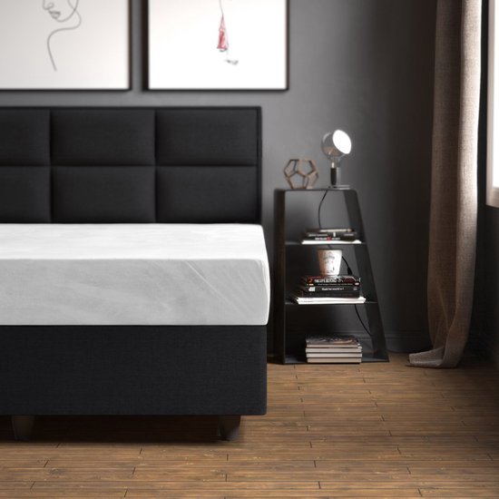 Wit hoeslaken op een bed met een zwart hoofdbord.