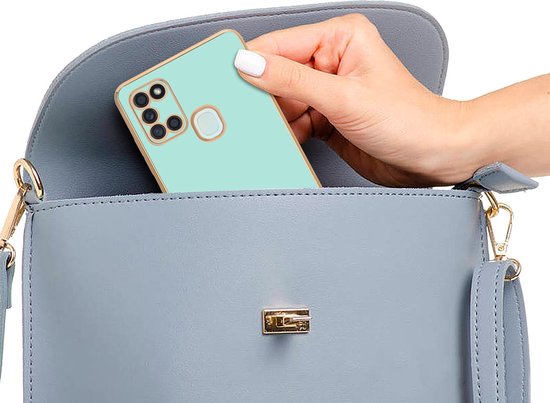 Hand plaatst mintgroen telefoonhoesje met gouden rand in een blauwe handtas.