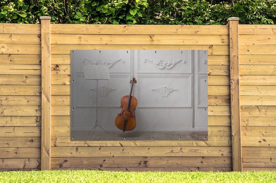 Tuinposter 180x120 cm - Tuindecoratie Een cello tegen een witte muur - Poster voor in de tuin - Buiten decoratie - Schutting tuinschilderij - Tuindoek muurdecoratie - Wanddecoratie balkondoek