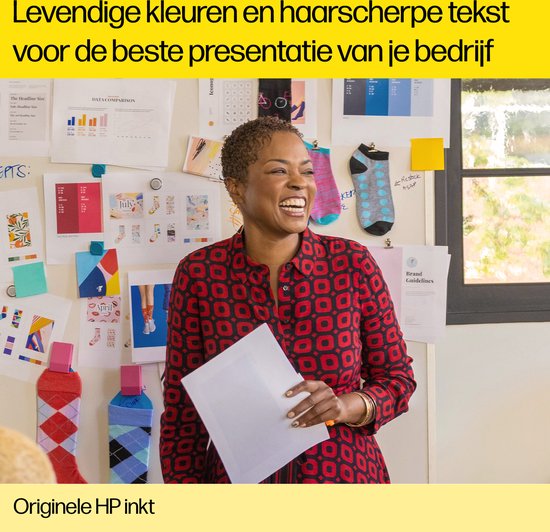 Vrouw met rood geruit shirt lacht en houdt papier vast voor een muur met prints.