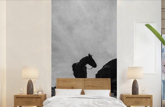 Zwart-wit fotobehang van een paard achter een slaapkamerbed met houten hoofdbord.