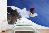 Papier peint photo vinyle - Un skieur fait un saut depuis un rocher enneigé largeur 390 cm x hauteur 260 cm - Tirage photo sur papier peint (disponible en 7 tailles)