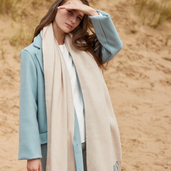 Model met lichtblauwe jas en beige sjaal, met de hand voor het gezicht.