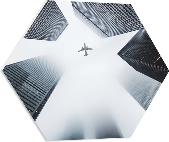 WallClassics - PVC Schuimplaat Hexagon - Vliegtuig vliegend tussen Gebouwen - 60x52.2 cm Foto op Hexagon (Met Ophangsysteem)