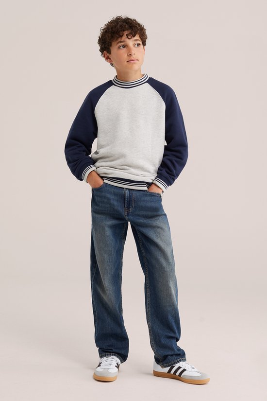 Jongen in donkerblauwe loose fit jeans, gestreepte trui en sneakers.