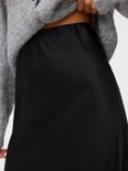 Détail de la taille haute d'une jupe longue noire en satin, portée avec un pull gris.