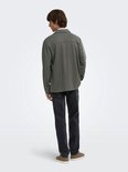 Mannelijk model met olijfgroene, lange mouwen oversized shirt en grijze jeans.