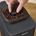 Hand verstelt maalgraad op zwarte Krups koffiemachine met koffiebonen.