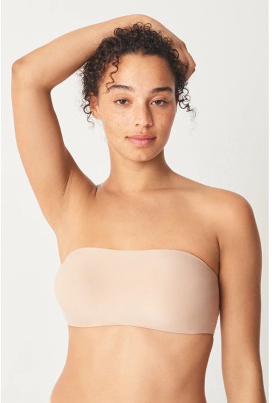 Model met krullend haar draagt een huidkleurige bandeau bh.