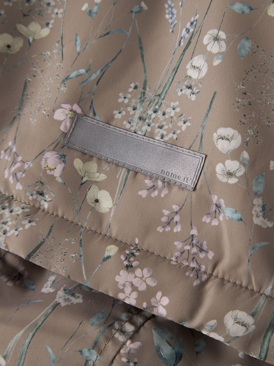 Beige jas met een all-over bloemenprint in zachtroze, lichtgroen en blauwtinten. Een zilverkleurig label met 'name it' is zichtbaar.