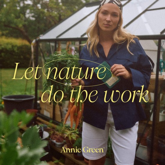 Vrouw met blonde haren, draagt een blauw jasje en witte shorts, houdt wortels vast in de tuin.