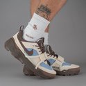 Gedetailleerde foto van een man die Nike Travis Scott sneakers draagt in gebroken wit, lichtblauw en bruin.