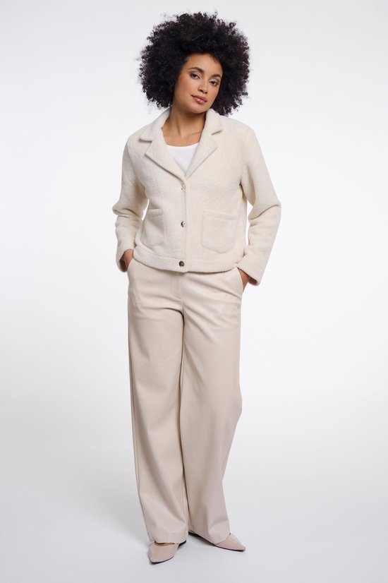 Le mannequin porte une veste en tricot blanc cassé avec deux poches et des boutons dorés, associée à un pantalon blanc cassé.
