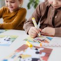 Kind met bruine vest gebruikt een gele stempelstift op een Bluey kaart met een hond.