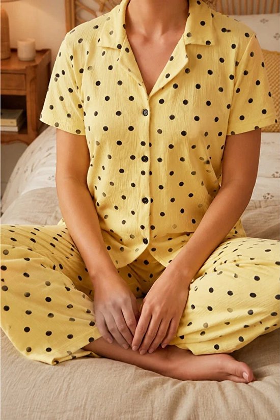 Gedetailleerde opname van een gele pyjamaset met zwarte polkadots, korte mouwen en lange broek.