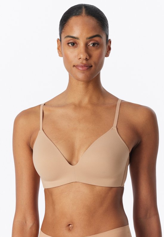 Close-up van een beige, naadloze beugel-vrije bh met diepe V-hals en dunne bandjes, gedragen door een model.