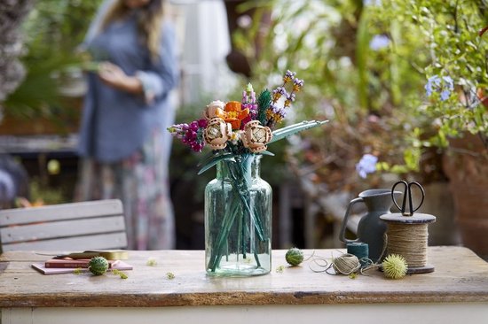 Een vaas met een boeket van LEGO bloemen in verschillende kleuren, waaronder oranje en paars, op een houten tafel.