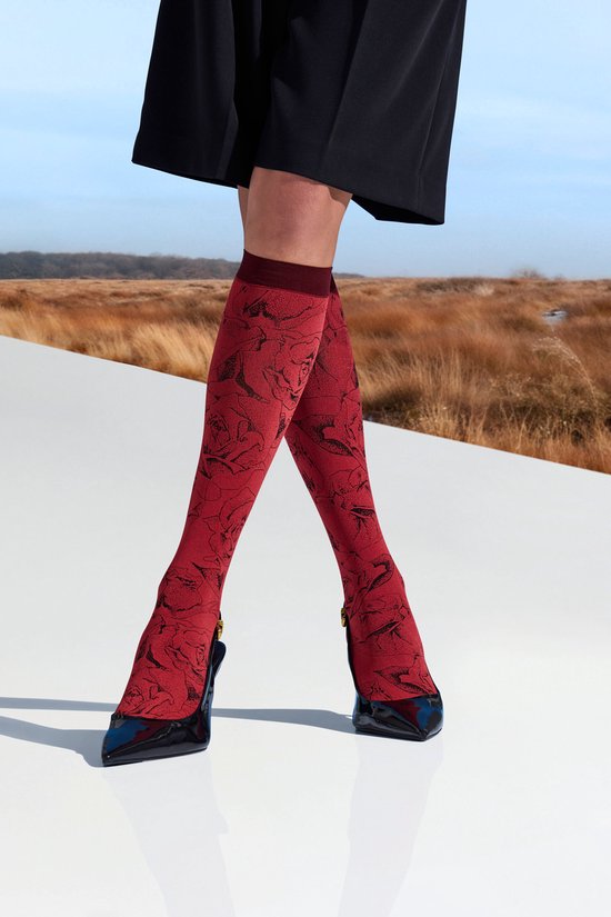 Model met rode kniekousen met zwarte rozenprint, hoge zwarte schoenen en zwarte rok.