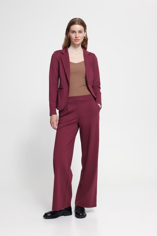 Model in een bordeauxrode pantalon en blazer met bruine top.