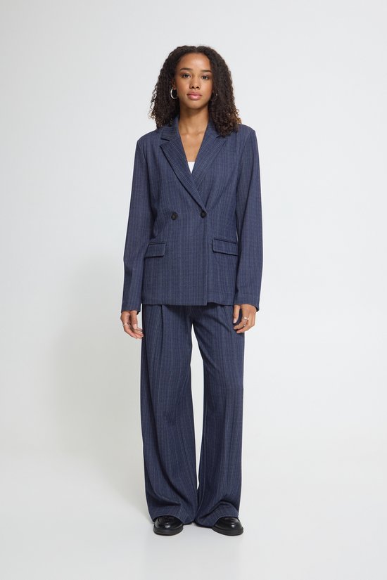 Model draagt een donkerblauwe krijtstreep blazer en bijpassende wijde broek.