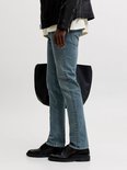 Zijzicht van een man in blauwe slim fit jeans met lichte wassing, zwarte bikerjas en leren tas.