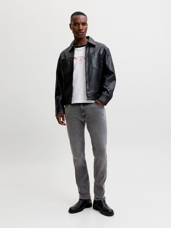 Man met zwarte leren jas, wit T-shirt en grijze jeans.