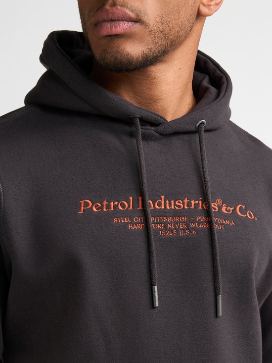 Detail van donkere hoodie met oranje opdruk 'Petrol Industries & Co.', met koordjes.