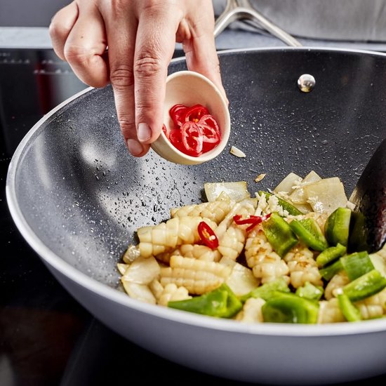 Persoon voegt rode pepers toe aan wok met groenten en vlees.