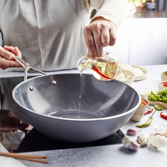 Persoon giet olie met pepers in een wokpan met groenten.