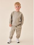 Jongen draagt een naturelkleurige sweater en joggingbroek met een subtiel lachend gezichtje op de borst.