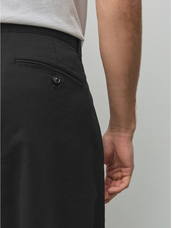 Close-up van de achterzak met knoop op een zwarte chino gedragen door een model.