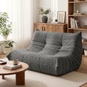 Grijze, zachte vloersofa met gewatteerde rug en zitvlak, geplaatst in een woonkamer.