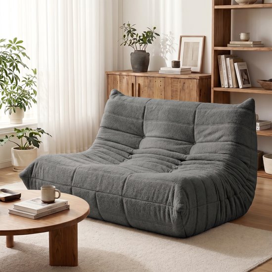 Grijze, zachte vloersofa met gewatteerde rug en zitvlak, geplaatst in een woonkamer.