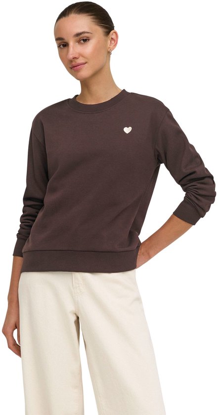 Model draagt bruine sweater met witte hart-applicatie, gecombineerd met witte broek.