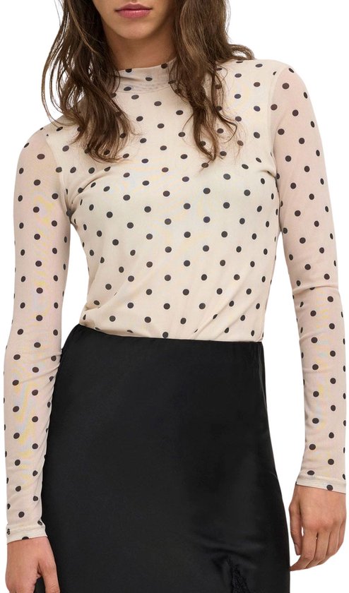 Femme portant un haut en résille crème à pois noirs et une jupe noire.