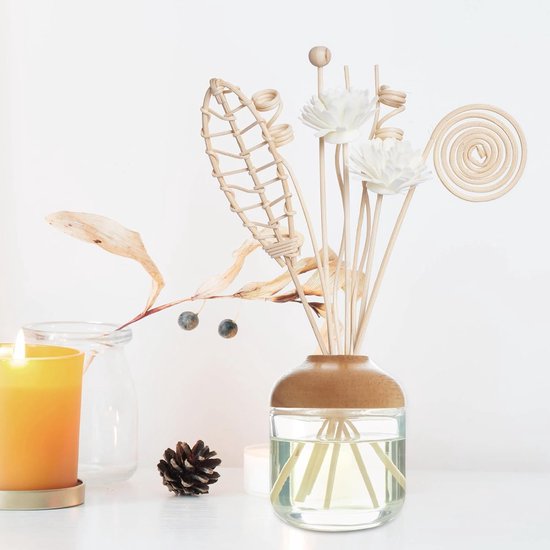 Een glazen diffuser met houten dop, gevuld met gele vloeistof en natuurlijke geurstokjes, met kaars en dennenappel.
