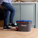 Persoon met spijkerbroek en sneakers gebruikt een Vileda spinmop met pedaalemmer in een keuken.