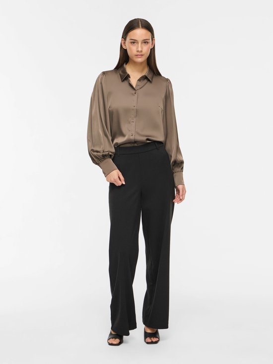 Model in taupe satijnen blouse met pofmouwen en zwarte broek.