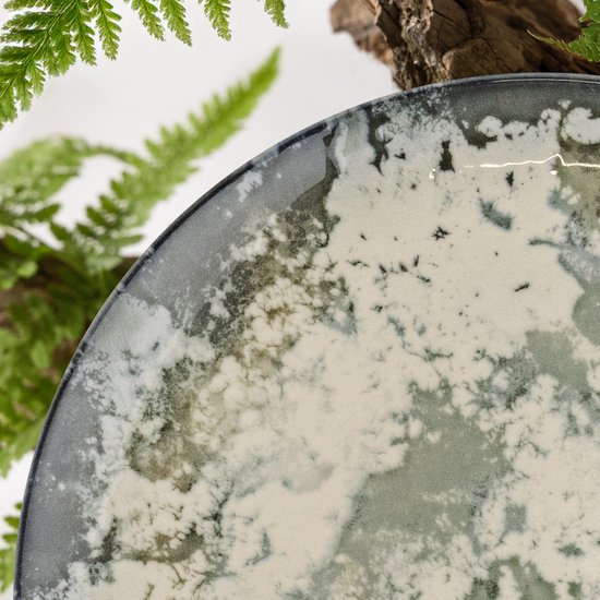 Detail van een plat bord met marmerachtig patroon in wit, grijs en donkerblauw, met varens.