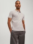 Man draagt beige polo met beige en witte boorden aan de mouwen en kraag.
