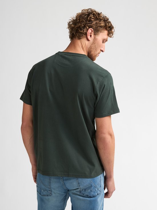 Donkergroen T-shirt, achterkant zichtbaar. Model draagt een spijkerbroek.