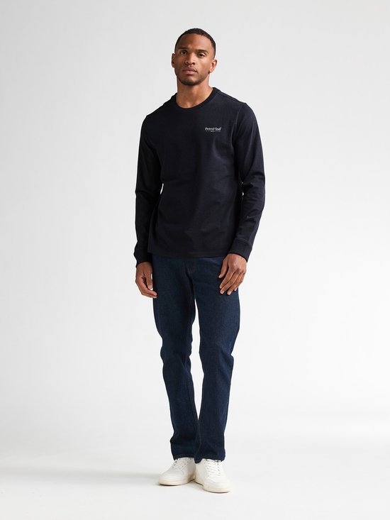 Man met donkerblauw longsleeve shirt met witte tekst op linkerborst en spijkerbroek.