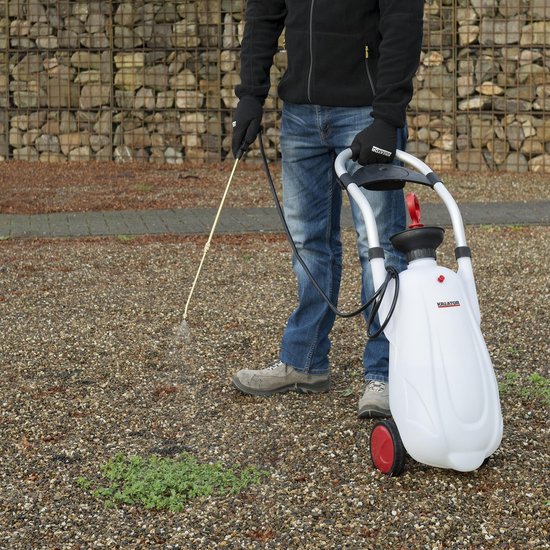 Man met jeans en zwarte jas gebruikt de witte trolley sproeier met rode wielen.