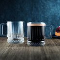 Glazen bierpul gevuld met donker bier en een lege bijpassende pul met verticale ribbels en decoratieve rand.