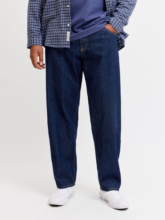 Man draagt donkerblauwe jeans met een openvallende geruite blouse.