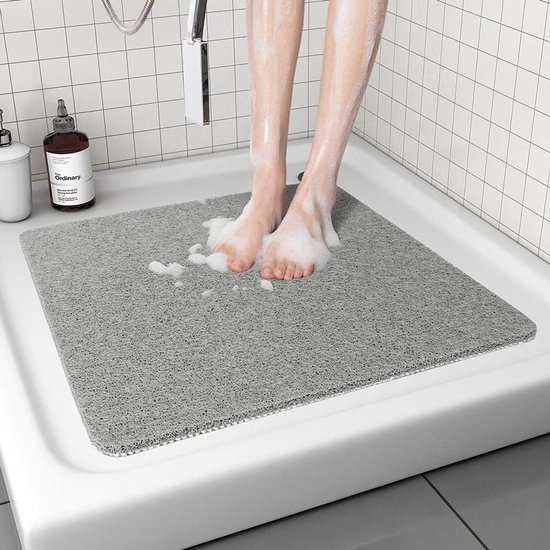 Voeten van een persoon met zeepbellen op een grijze antislip douchemat in een douchebak.