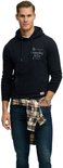 Model in donkerblauwe hoodie met geruit overhemd om middel geknoopt en jeans.